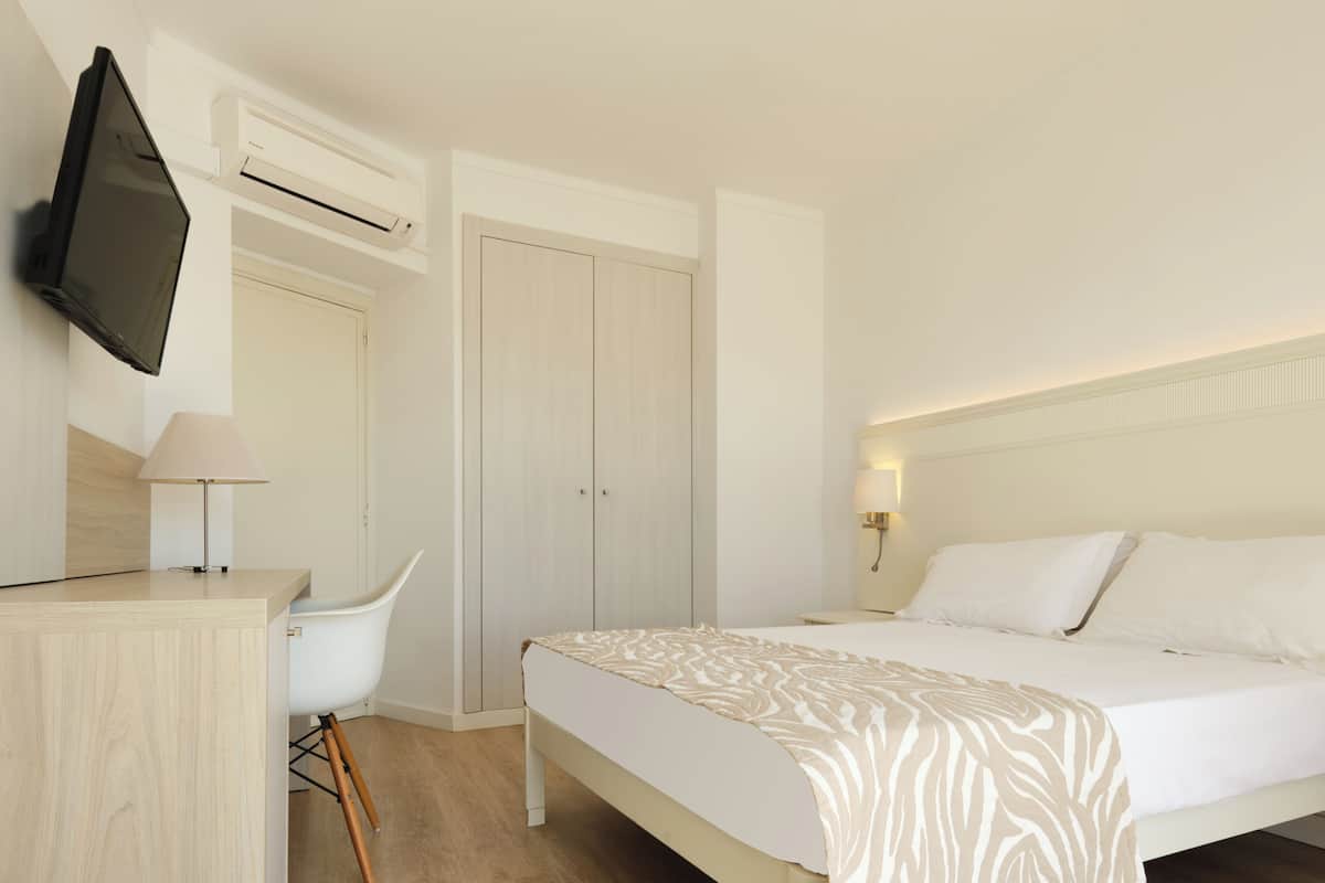 Una habitación de hotel con cama, escritorio con lámpara, televisor y armario.