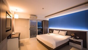 Una habitación de hotel moderna con una cama grande, mesitas de noche, un televisor y un ventanal corredero que da a un balcón.