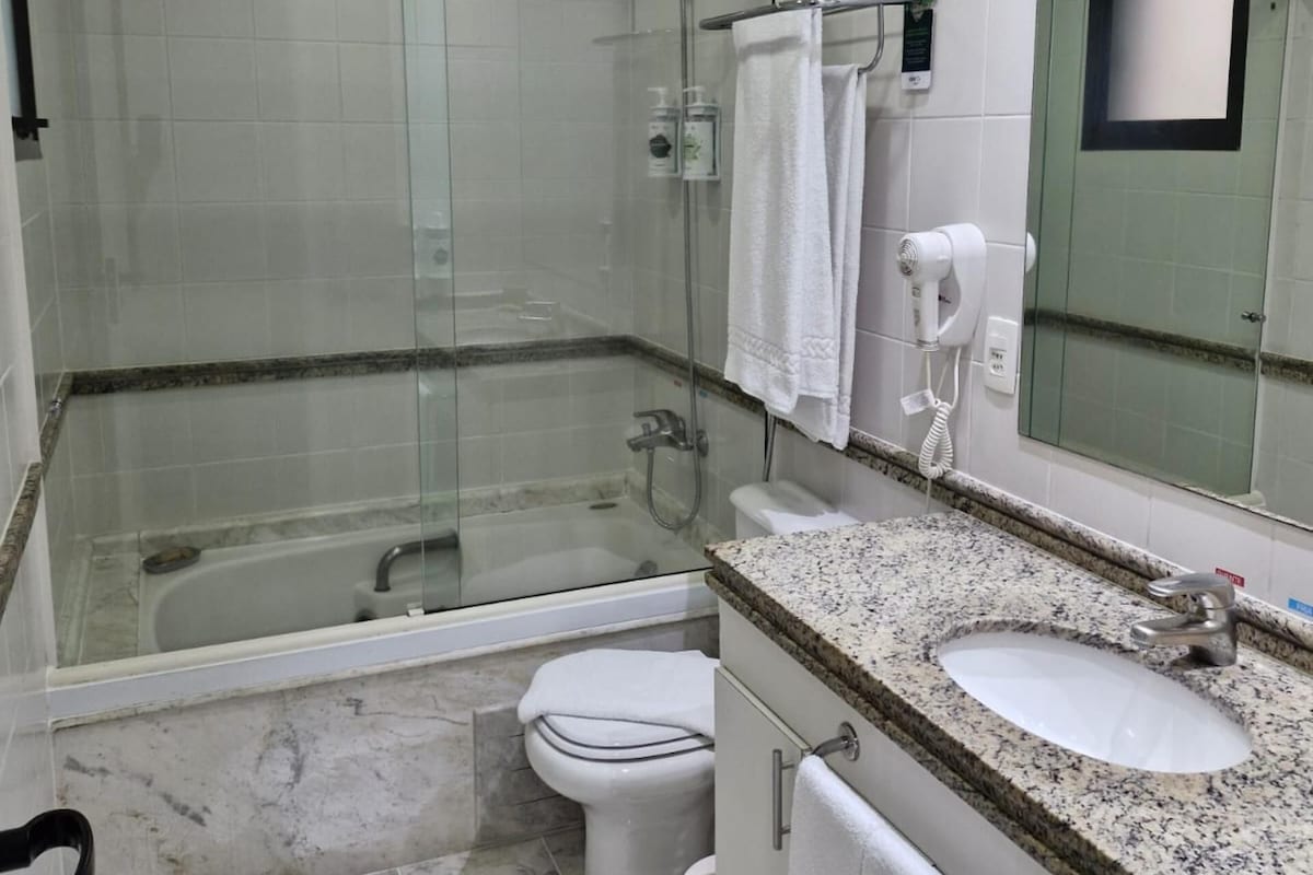 Un baño moderno con ducha de vidrio, inodoro independiente, lavabo con encimera de granito y un espejo grande.