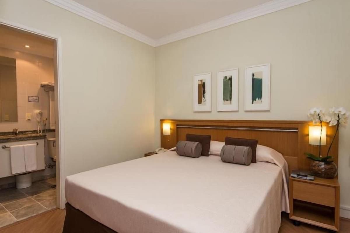 Une chambre d’hôtel comprenant un lit, une table de chevet, une lampe et une œuvre d’art accrochée au mur.