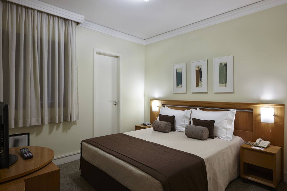 Ein Hotelzimmer mit Bett, Nachttischen, Fernseher und Kunstwerk an der Wand.