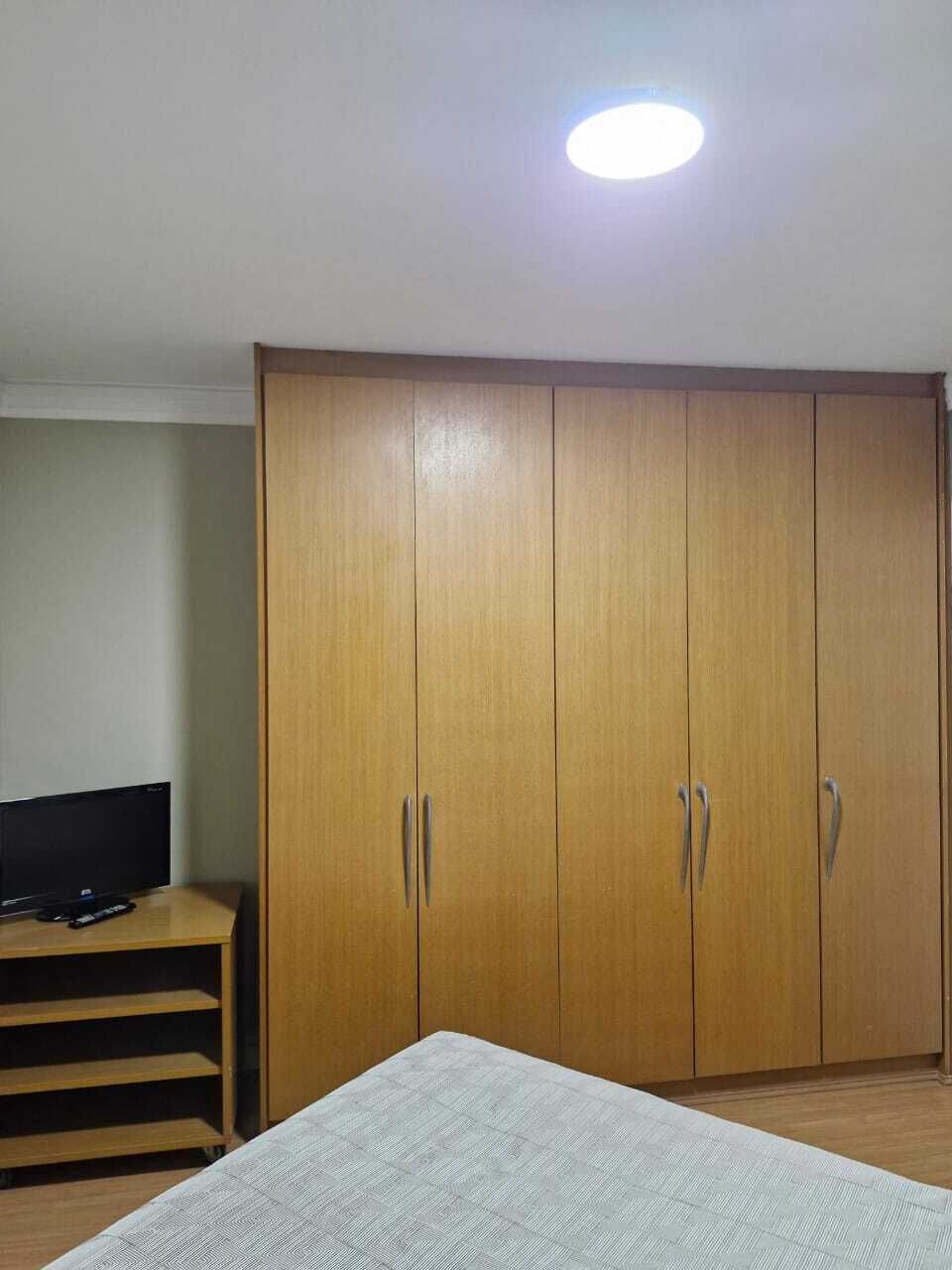 A room with a bed, a wardrobe, a television on a stand, and a ceiling light.