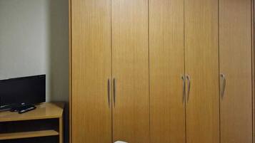A room with a bed, a wardrobe, a television on a stand, and a ceiling light.