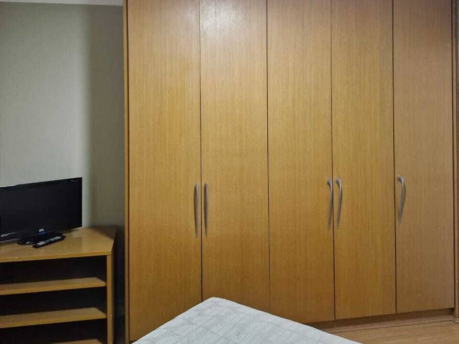 A room with a bed, a wardrobe, a television on a stand, and a ceiling light.