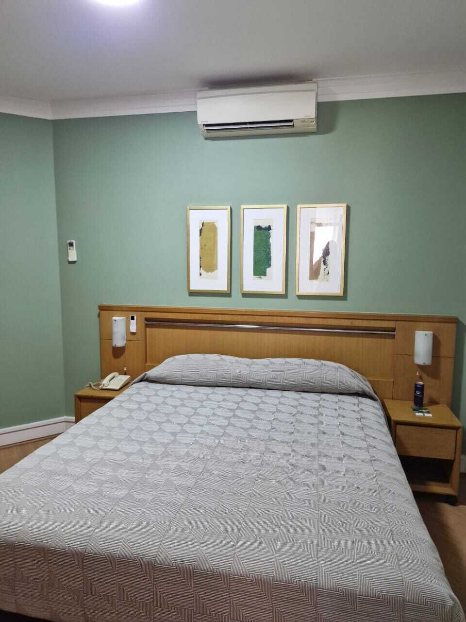 A hotel room with a bed, a nightstand, a phone, a lamp, and three framed pictures on the wall.