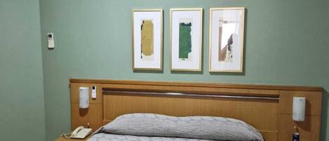 A hotel room with a bed, a nightstand, a phone, a lamp, and three framed pictures on the wall.