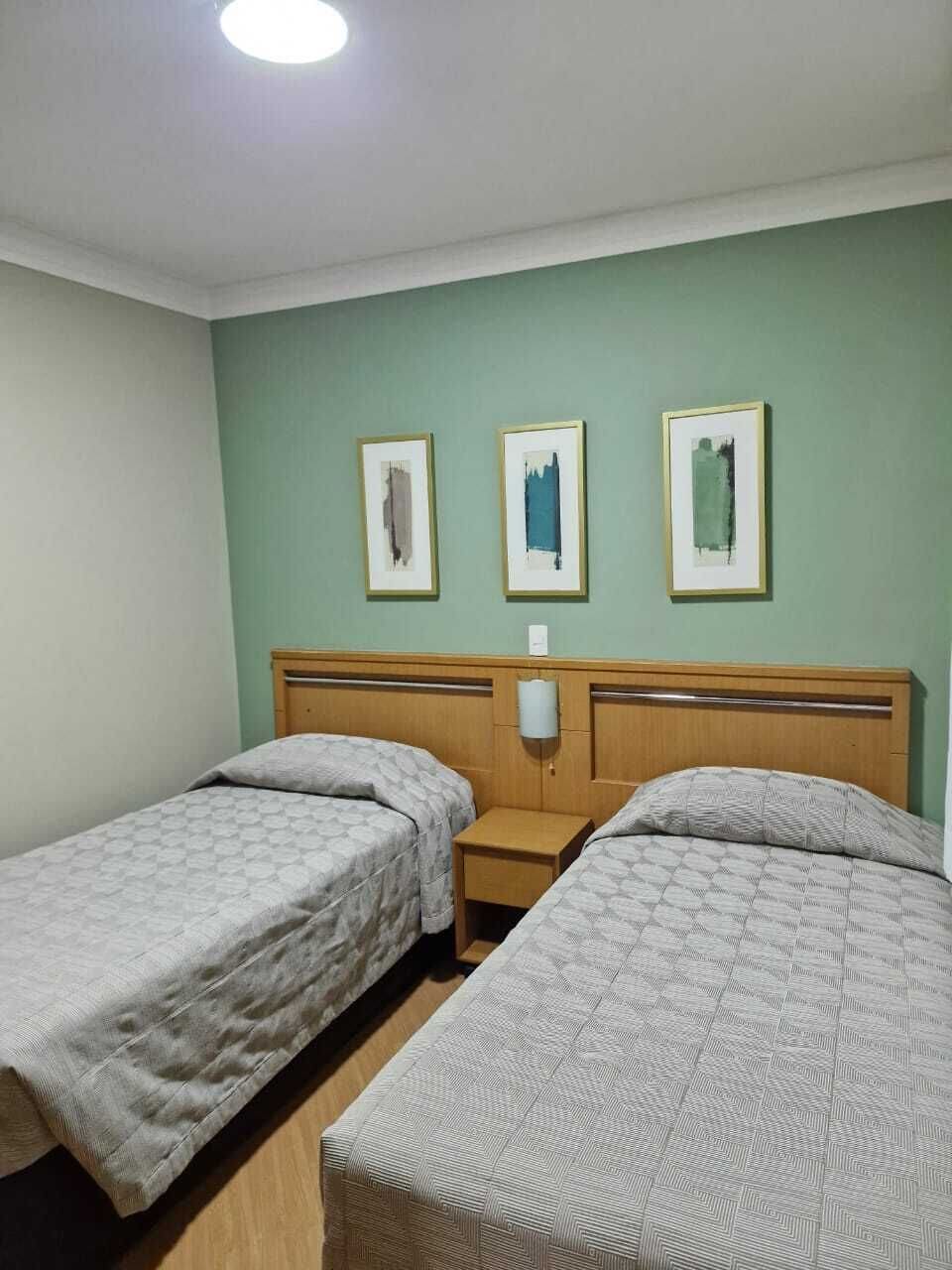 Una stanza con due letti, una testiera in legno, un comodino e tre opere d'arte appese al muro.