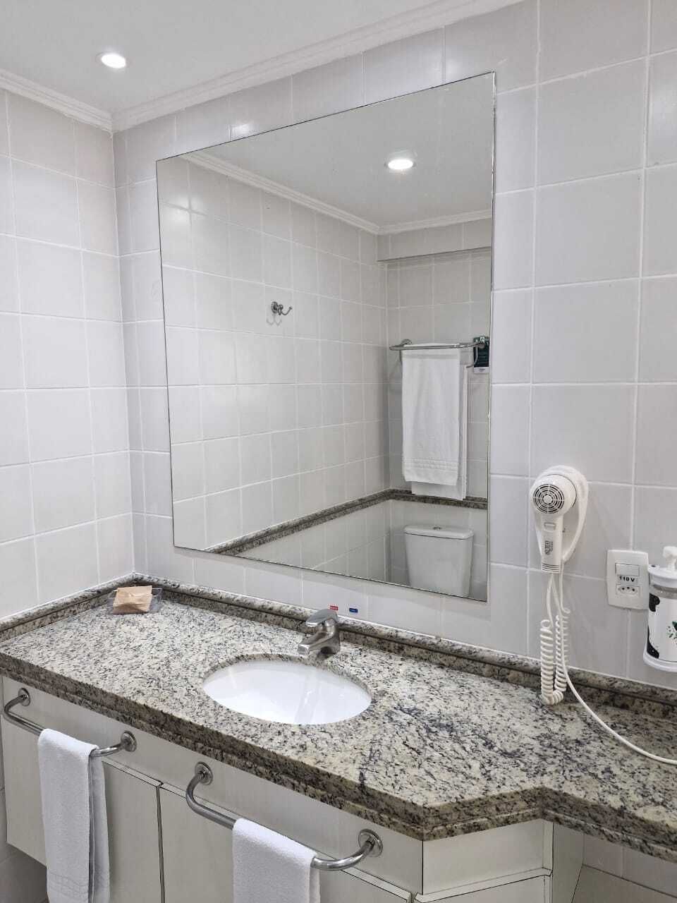 A bathroom with a granite countertop sink, a large mirror, a hairdryer, and a towel rack.