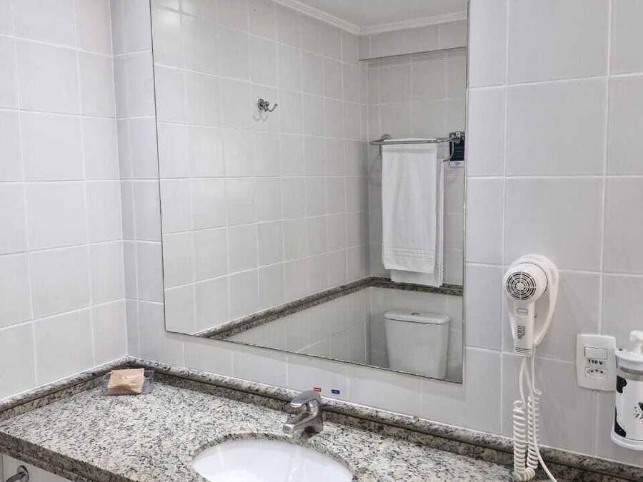 A bathroom with a granite countertop sink, a large mirror, a hairdryer, and a towel rack.