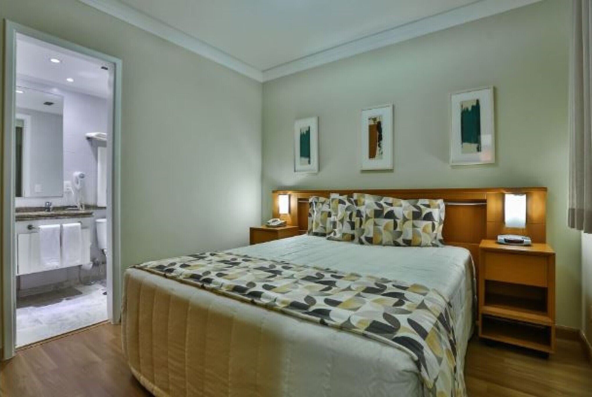 A hotel room with a bed, bedside tables, a mirror, and artwork on the wall.