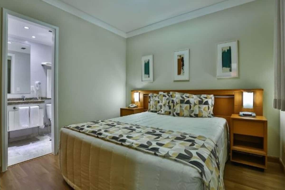 A hotel room with a bed, bedside tables, a mirror, and artwork on the wall.