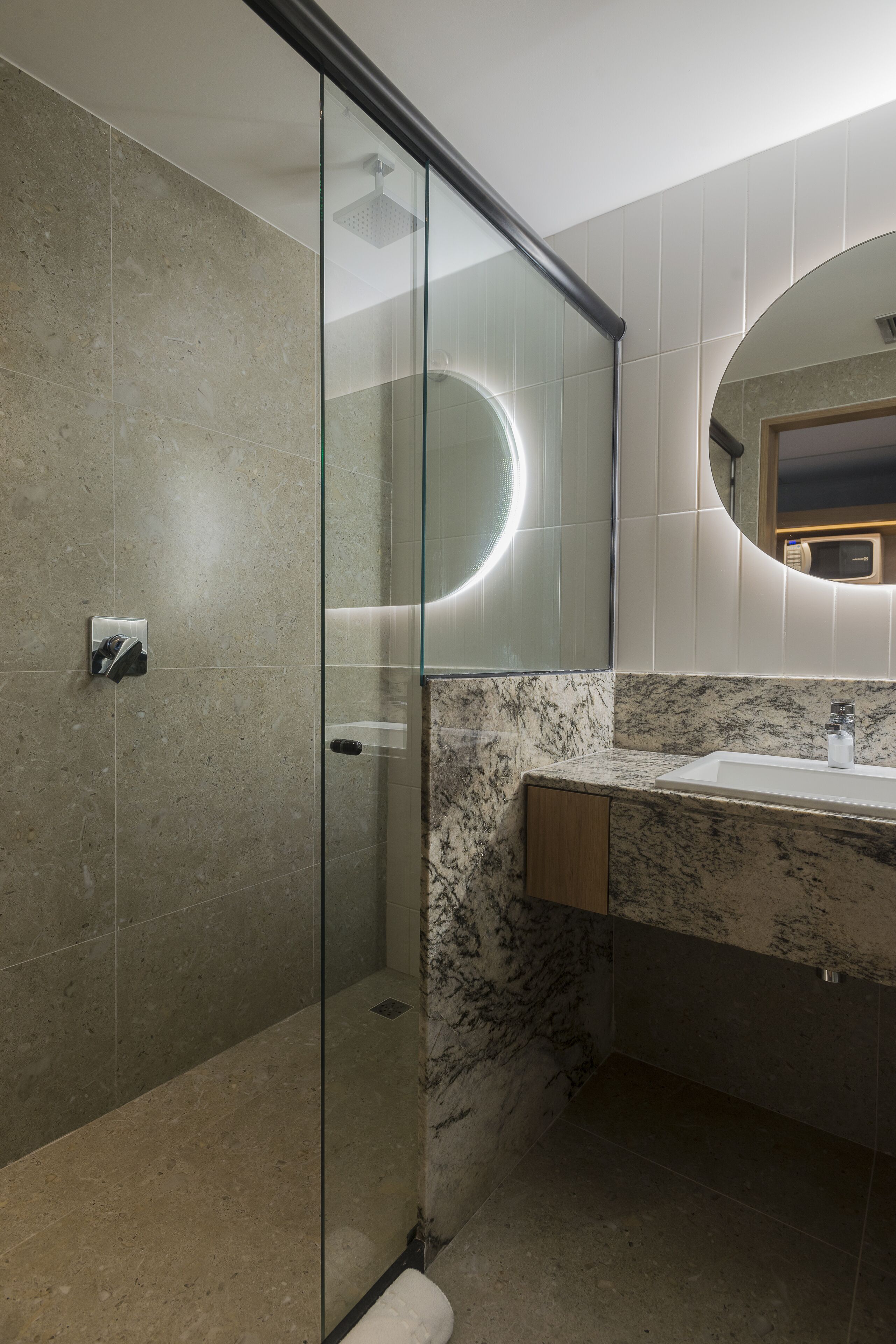 A modern bathroom with a glass-enclosed shower, a marble sink, and a large mirror.