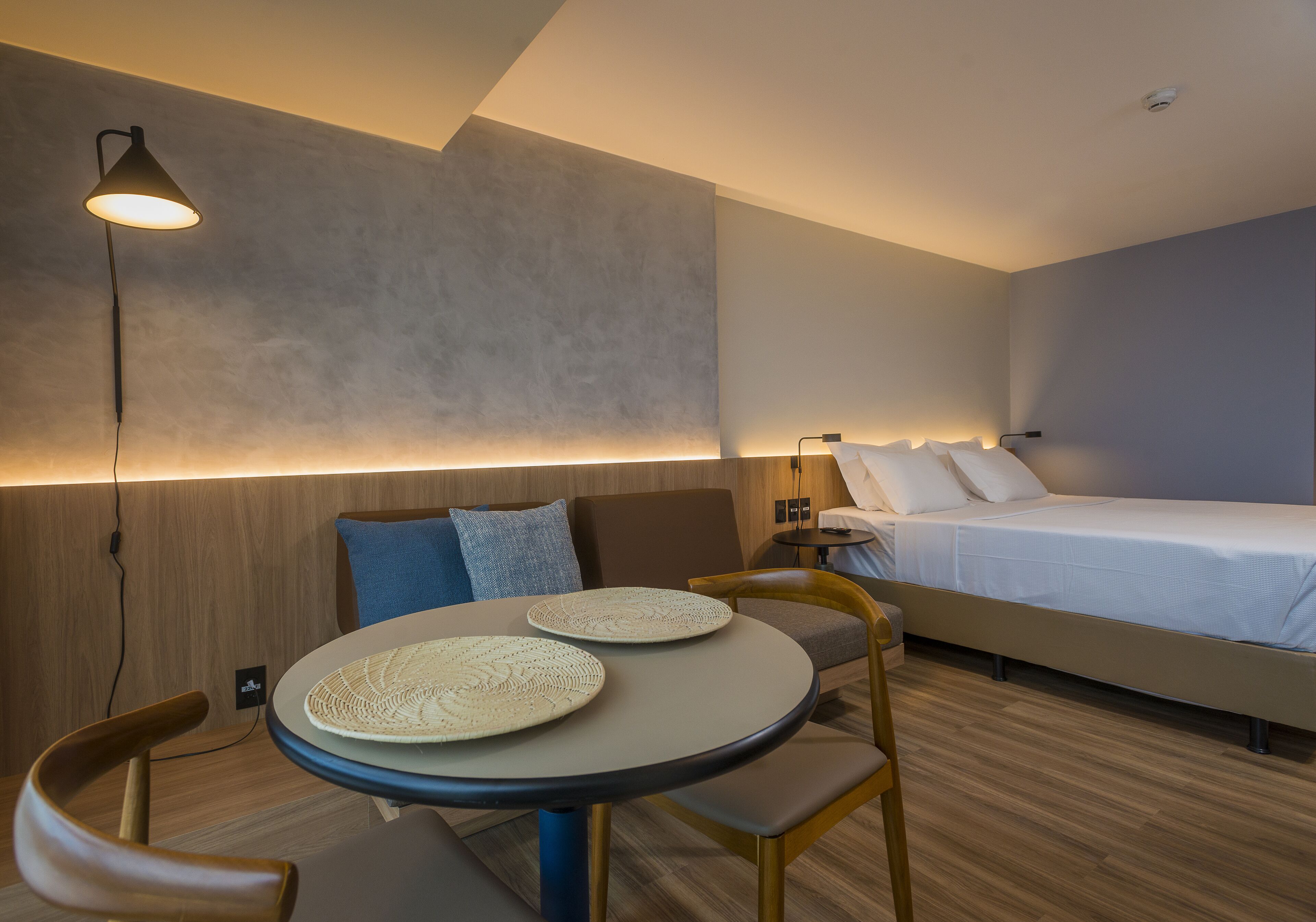 Una habitación de hotel moderna con una mesa redonda, dos sillas, una cama y una mesita de noche.