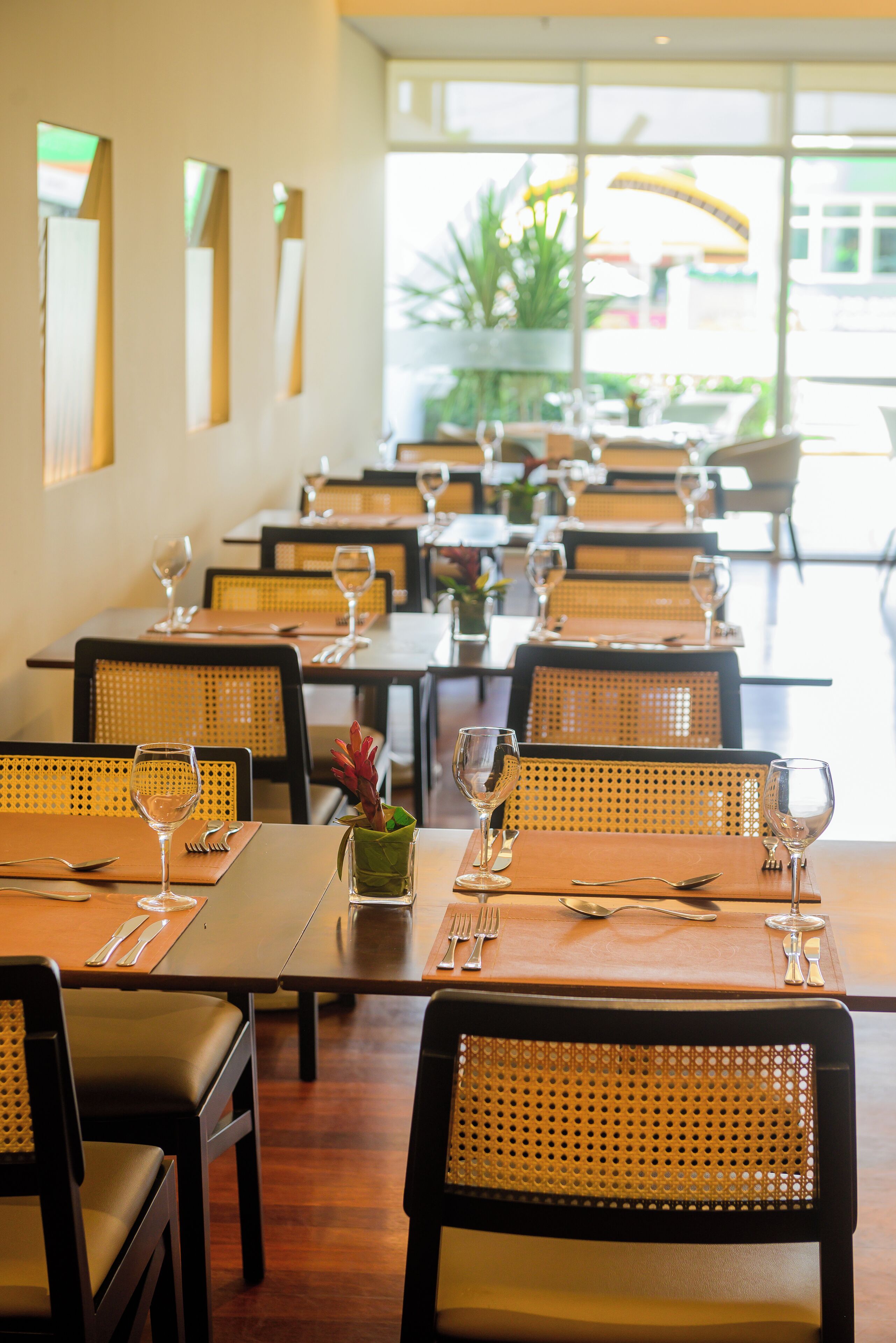 Un restaurante con mesas dispuestas para comer, con sillas de mimbre y vistas al exterior.