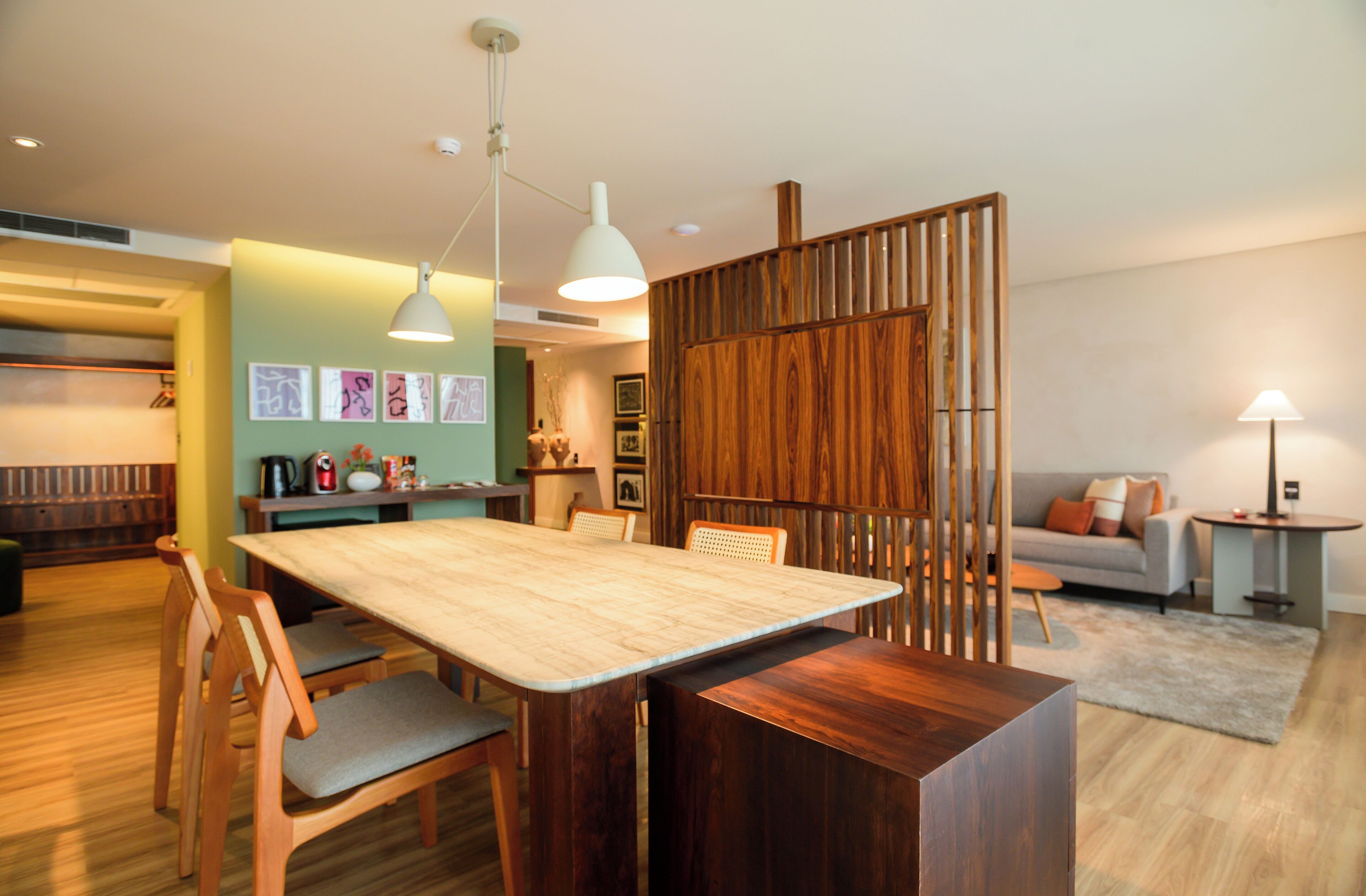 Uma área de refeições moderna com mesa e cadeiras de madeira, um painel com ripas verticais e um sofá ao fundo.