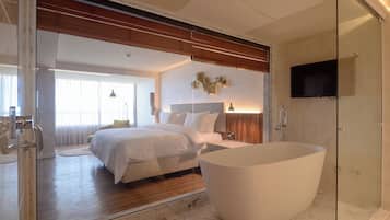Quarto moderno com cama grande, box de vidro para o chuveiro e uma banheira espaçosa.