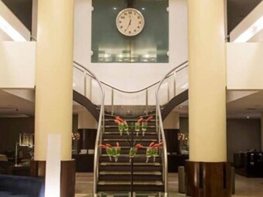 Eine Lobby mit Glastisch, einer Uhr und einer Treppe mit roten Blumen.