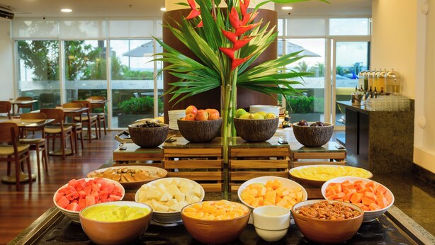 A buffet with various fruits and vegetables, wooden chairs, and a large window in the background. - Hotel Luzeiros Fortaleza (Fortaleza)