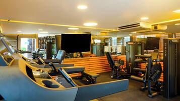 Un gimnasio con diversos equipos de ejercicio, como cintas de correr, máquinas de pesas y una pantalla de televisión.