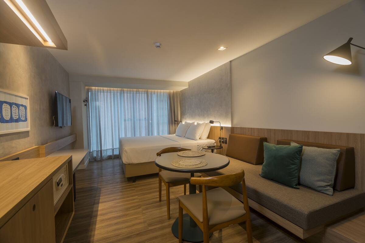 A hotel room with a bed, a sofa, a dining table with chairs, a desk, and a television.