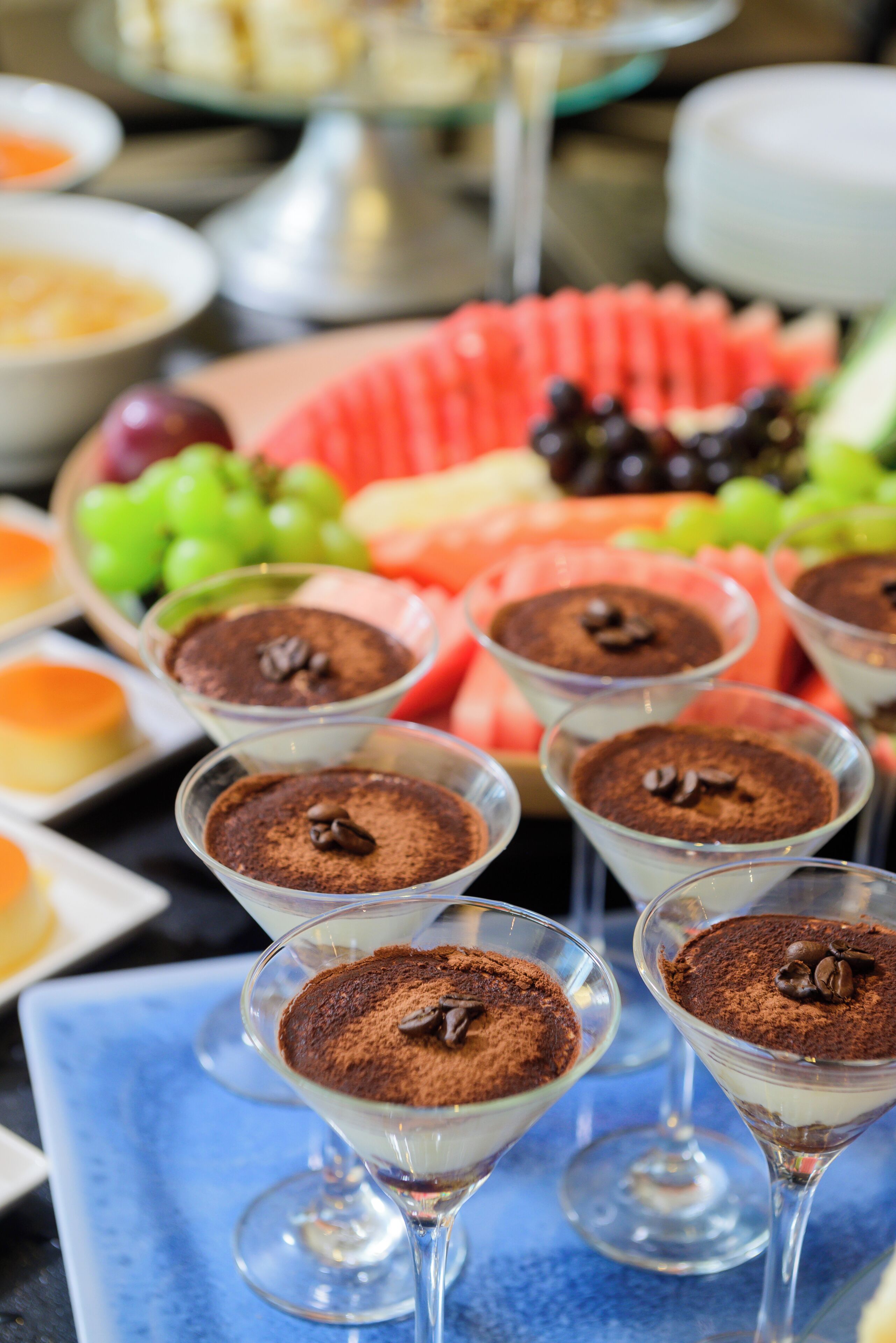 Una mesa con vasos de postres: tiramisú, sandía y uvas.