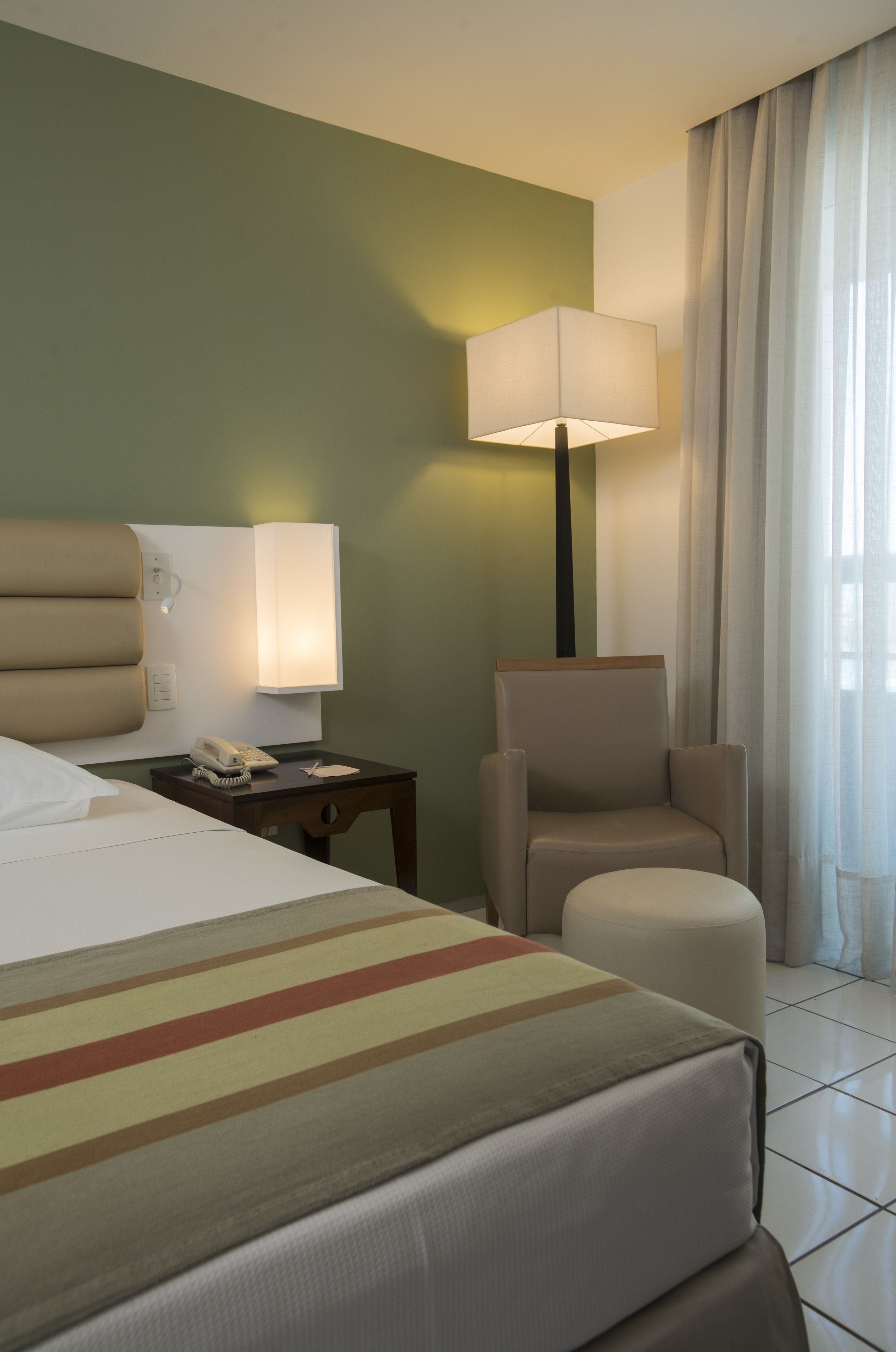 Une chambre d’hôtel comprenant un lit, une chaise, une table de chevet avec une lampe et un téléphone.