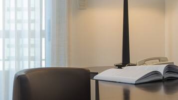 Una habitación de hotel con escritorio, lámpara, teléfono y un libro abierto.