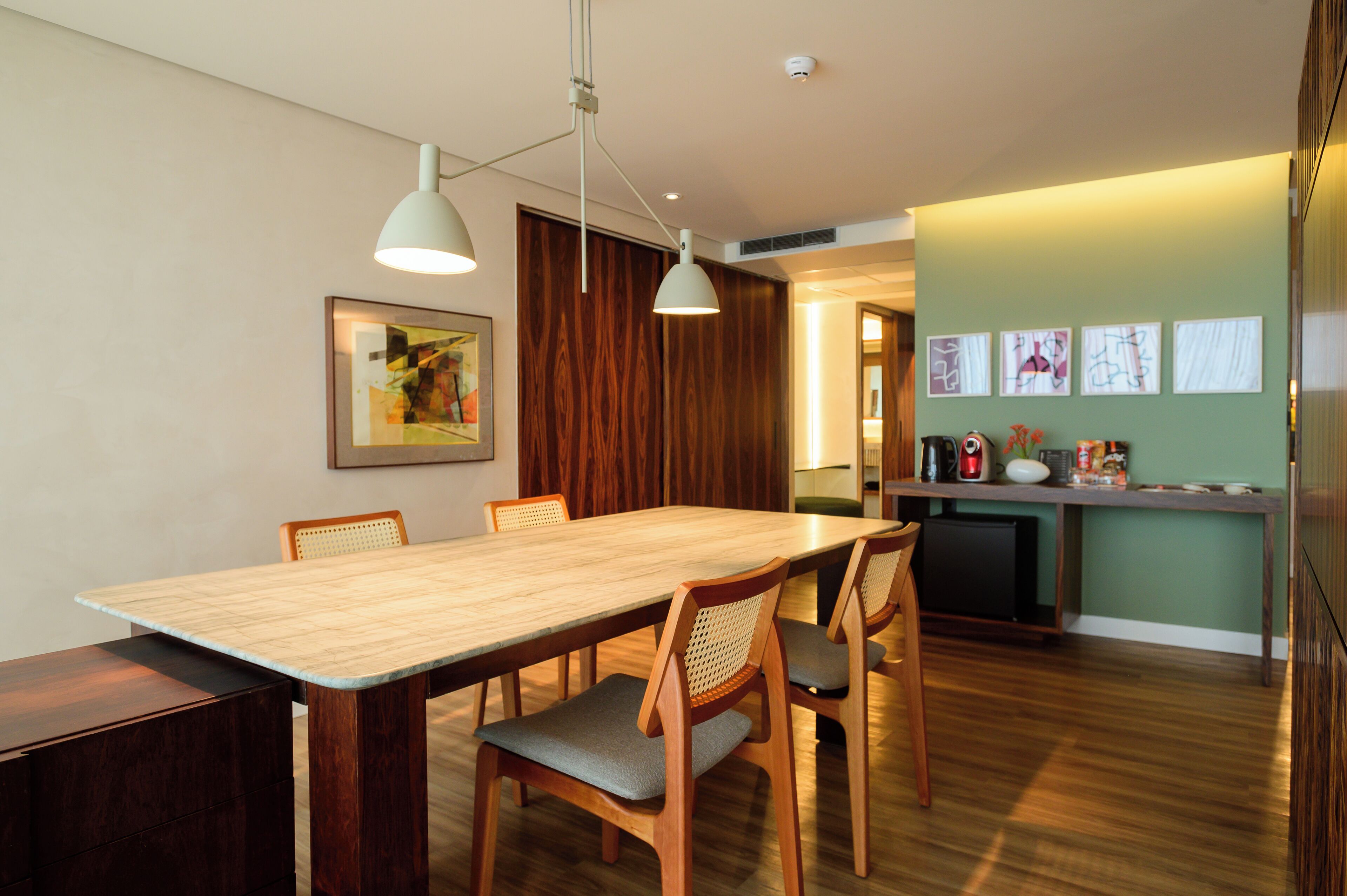 Un comedor con mesa y sillas de madera, una zona de cocina con refrigerador y armarios, y una pared decorada con cuadros.