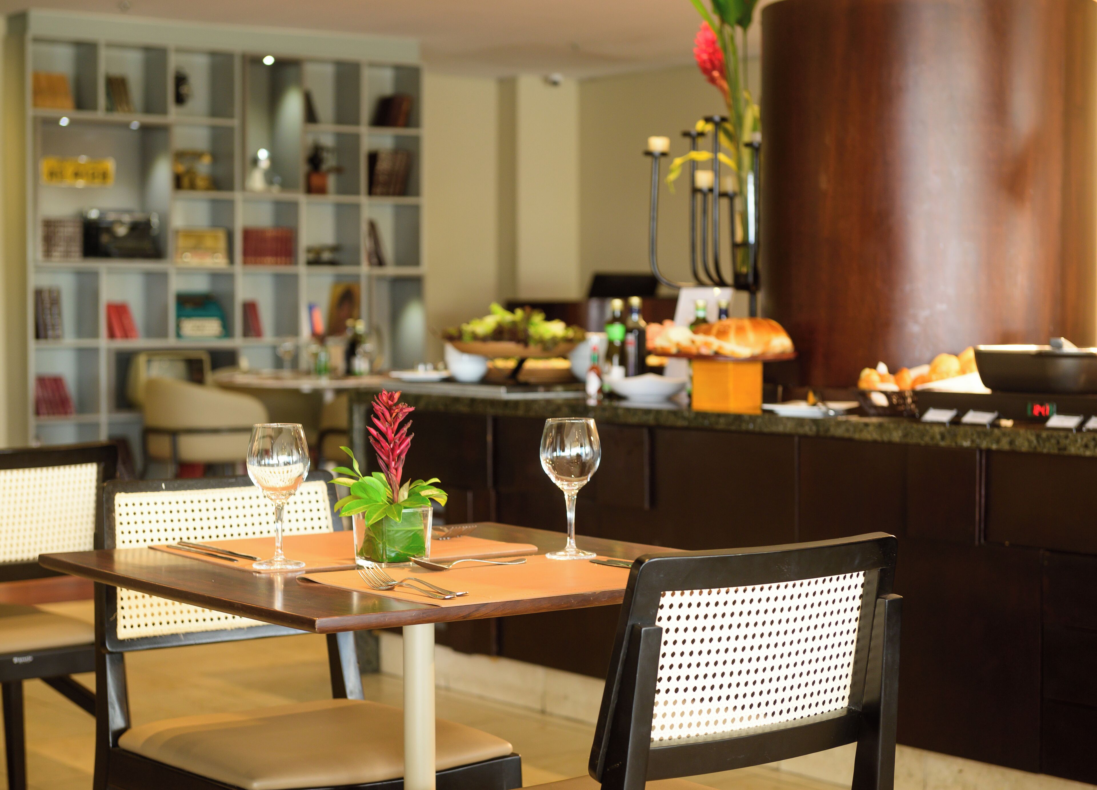 Een restaurant met een bar, eettafels met stoelen en een boekenkast op de achtergrond.