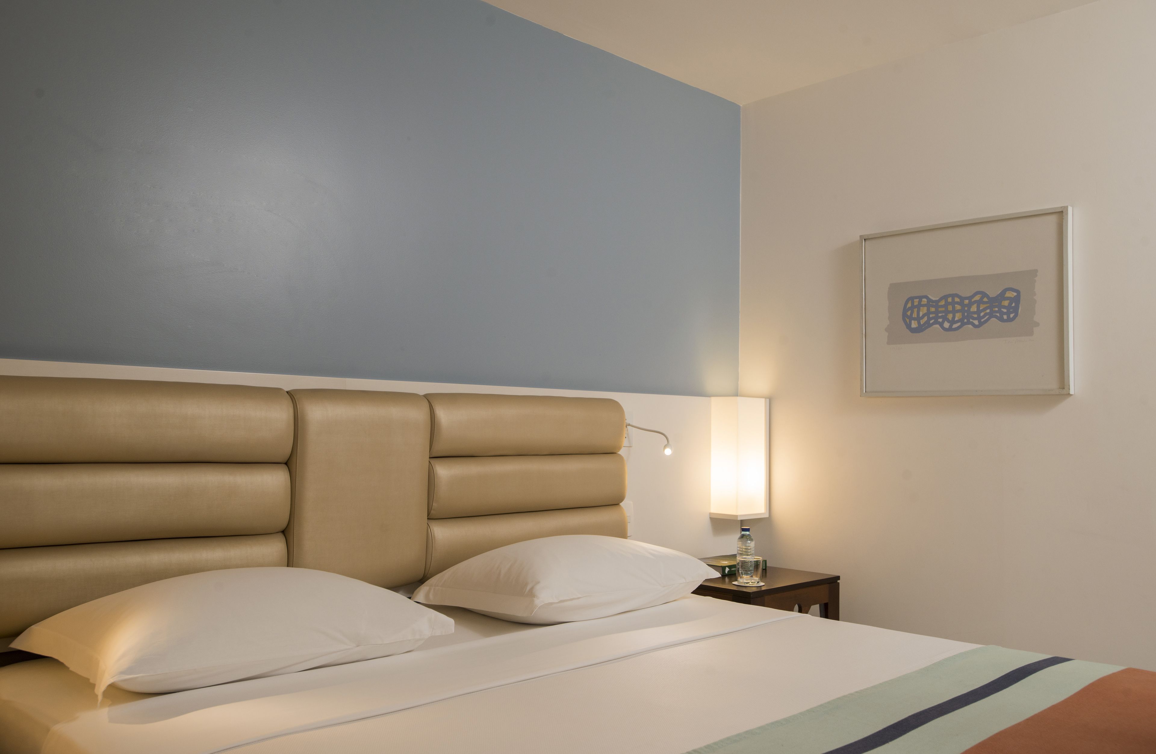 Una habitación de hotel con una cama, una mesita de noche, una lámpara y un cuadro en la pared.