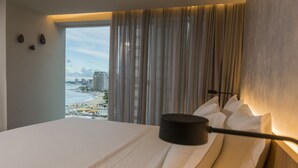 A hotel room with a bed, a view of the beach and buildings, and a lamp on the bedside table. - Hotel Luzeiros Fortaleza (Fortaleza)