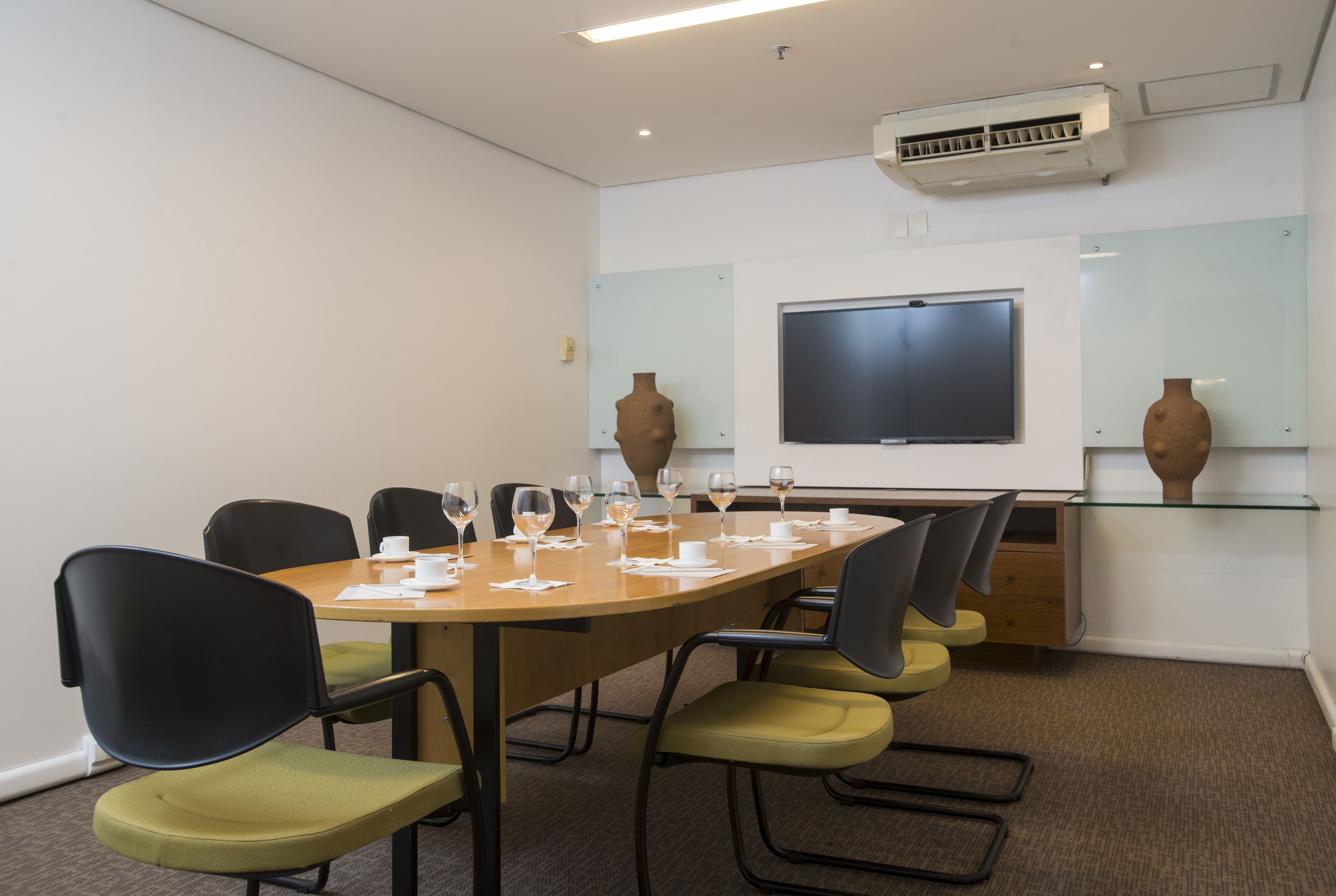 A conference room with a long table, chairs, a projector screen, and decorative vases.