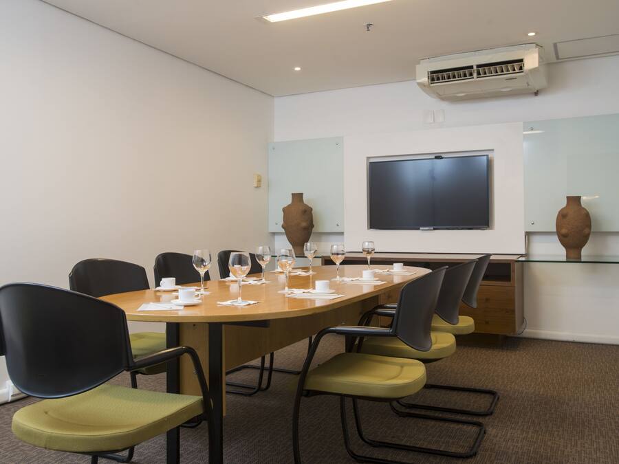 A conference room with a long table, chairs, a projector screen, and decorative vases.