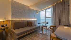 A modern hotel room with a sofa, a small round table, a lamp, and a view of the sea. - Hotel Luzeiros Fortaleza (Fortaleza)