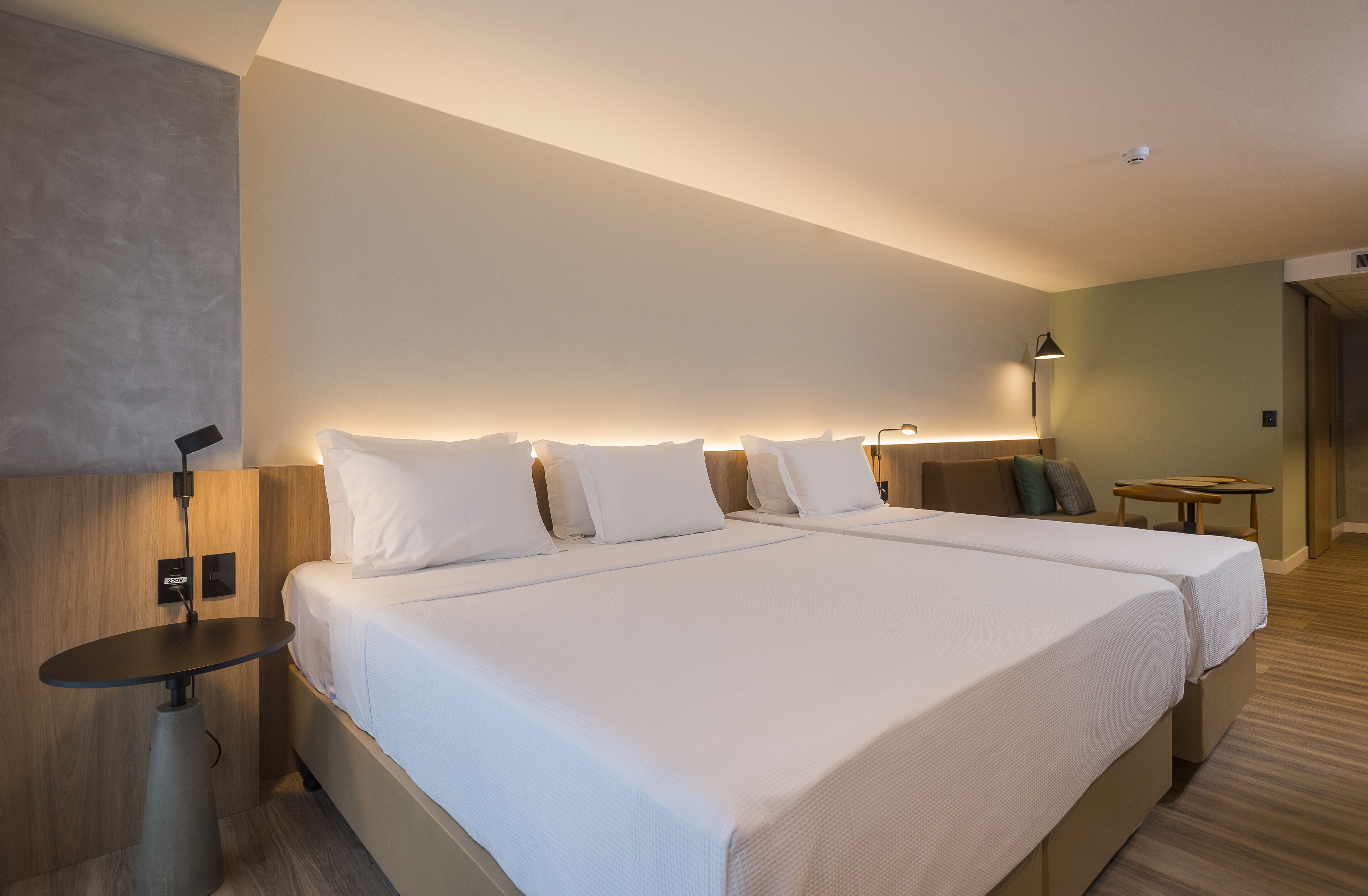 A hotel room with two beds, a desk, a lamp, and a small table.