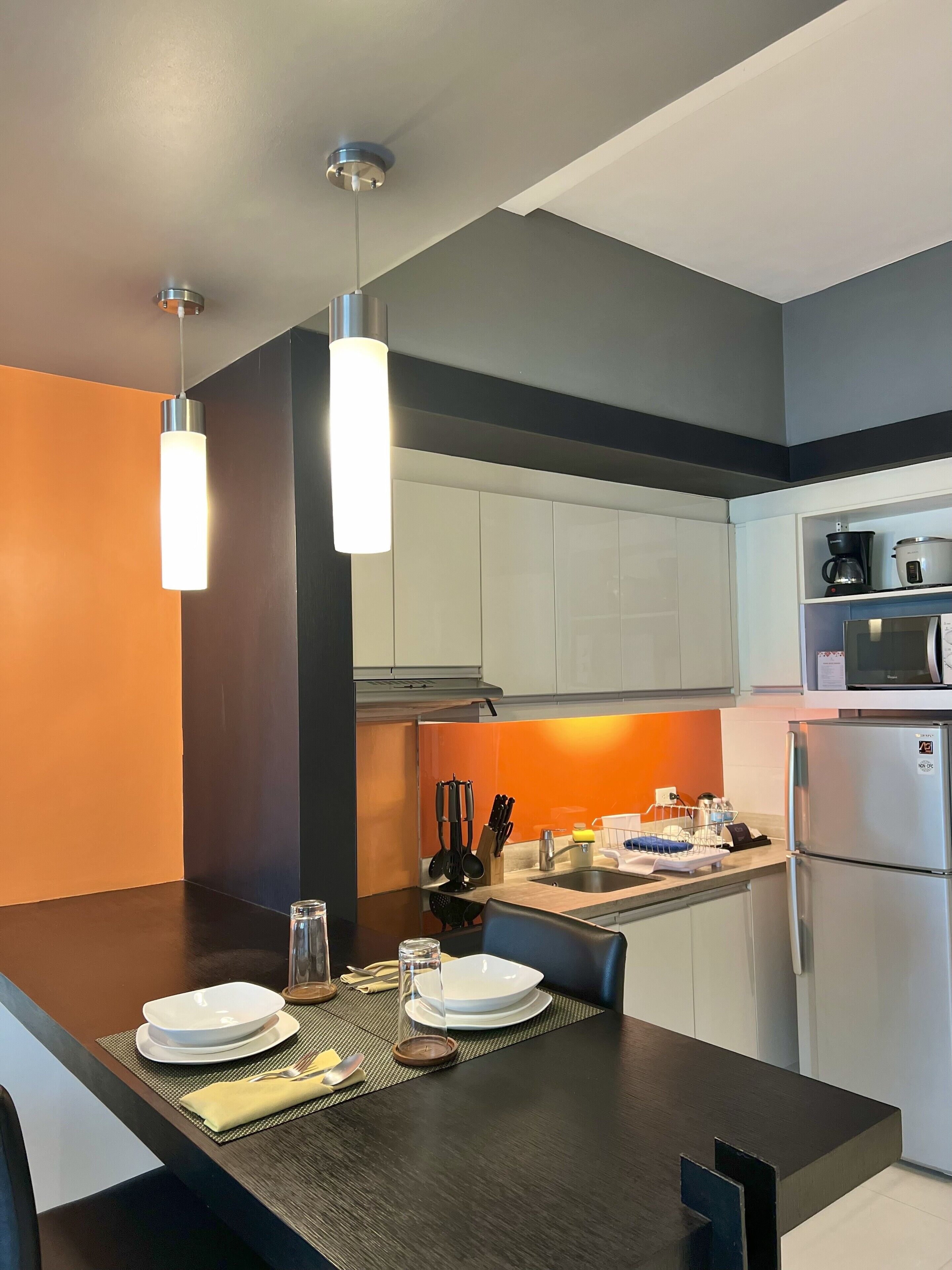 A modern kitchen with a dark wooden table set for dining, white cabinets, and a stainless steel refrigerator.