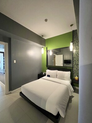 A modern hotel room with a large bed, a bedside table with a phone, a mirror, and a green accent wall. - KL Serviced Residences Managed by HII (Makati)