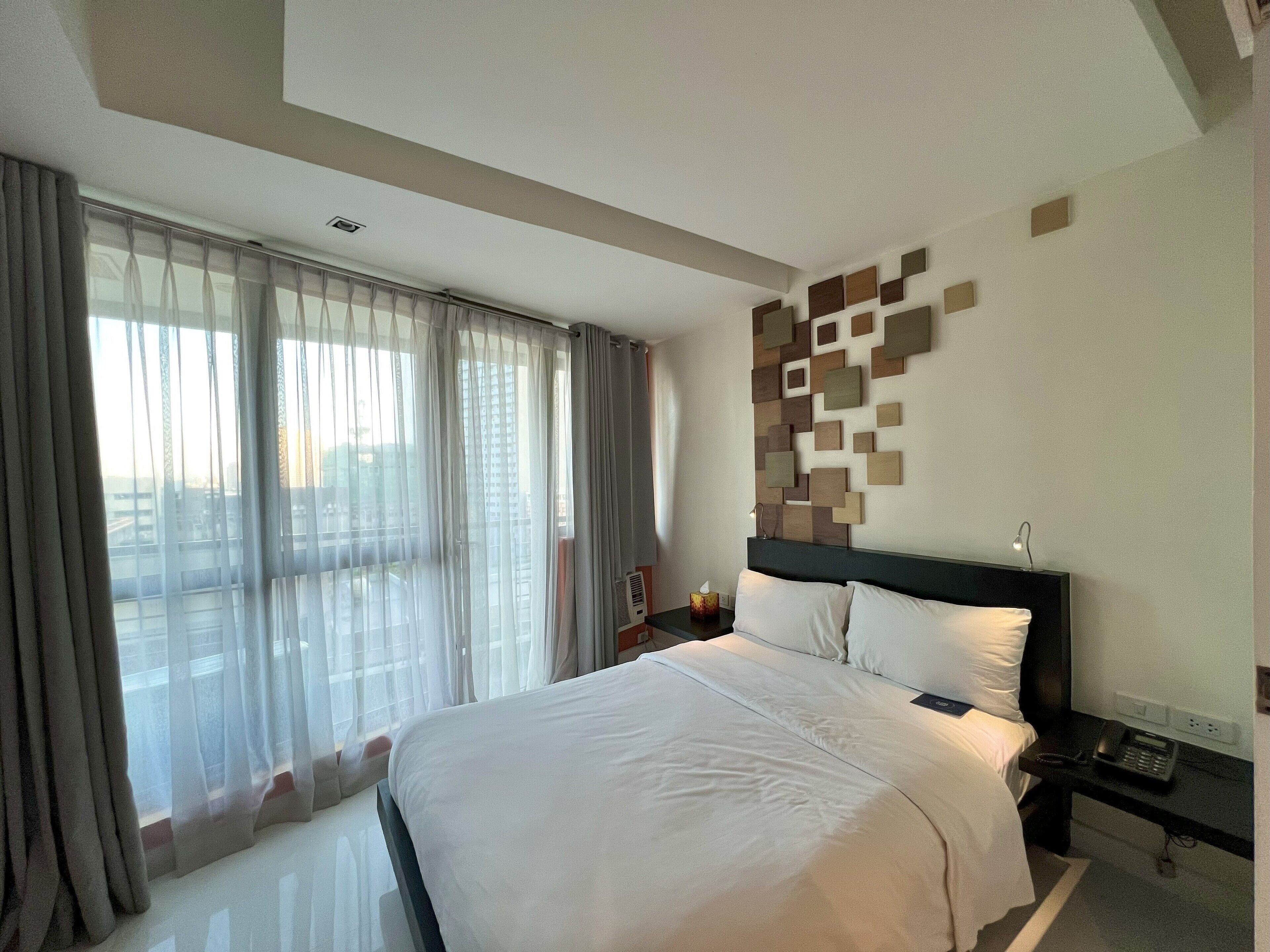 A hotel room with a large bed, a nightstand with a phone, and a wall-mounted light.