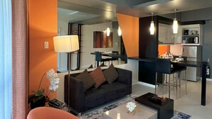 Ein modernes Wohnzimmer mit einer Couch, einem Couchtisch und einem Essbereich mit Stühlen. Im Hintergrund ist eine Küche zu sehen.
