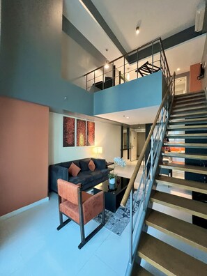 A spacious living area with a modern staircase, a sofa, and a coffee table. - KL Serviced Residences Managed by HII (Makati)