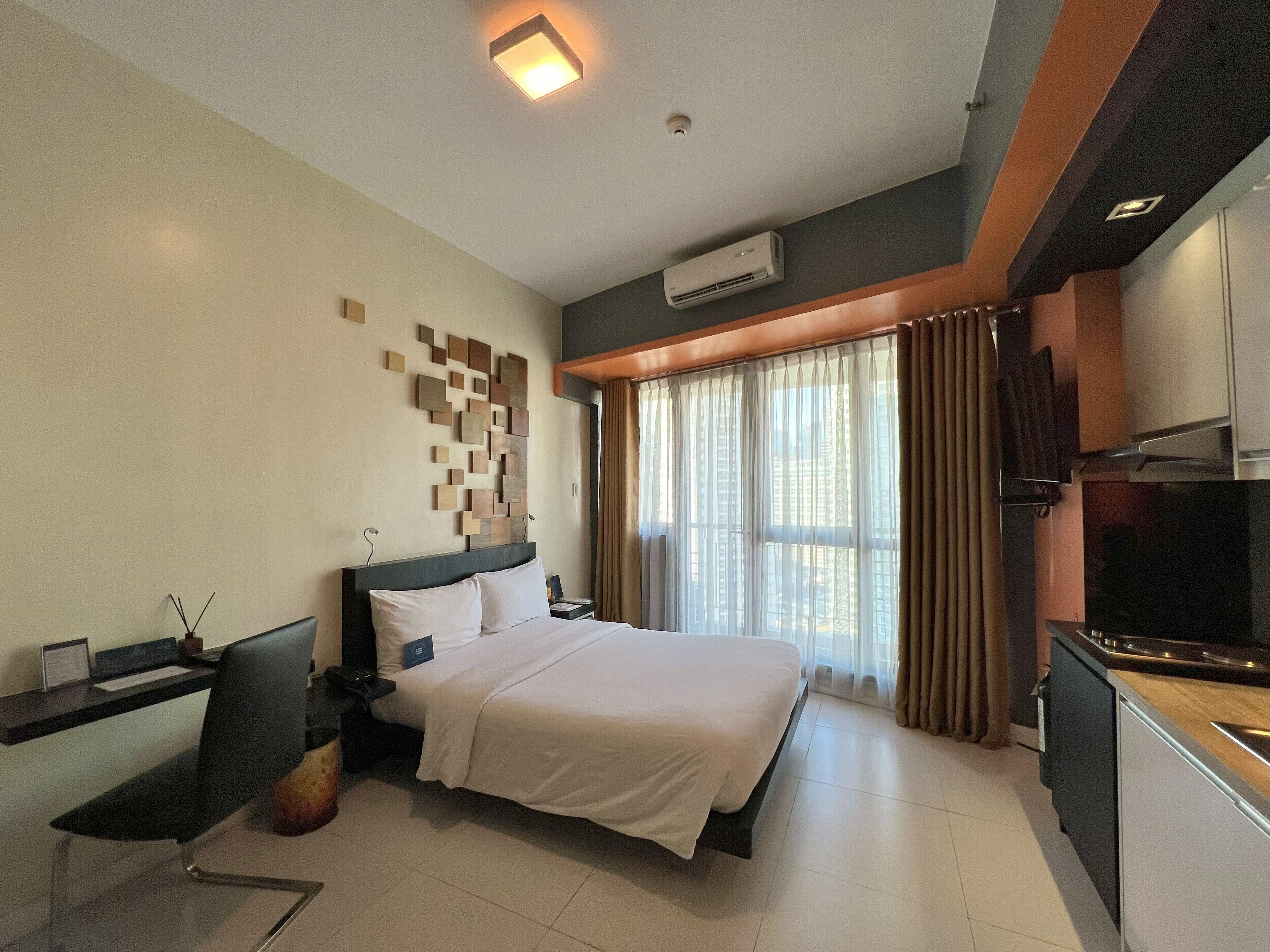 A modern hotel room with a large bed, a desk with a chair, a flat-screen TV, and a window with curtains.