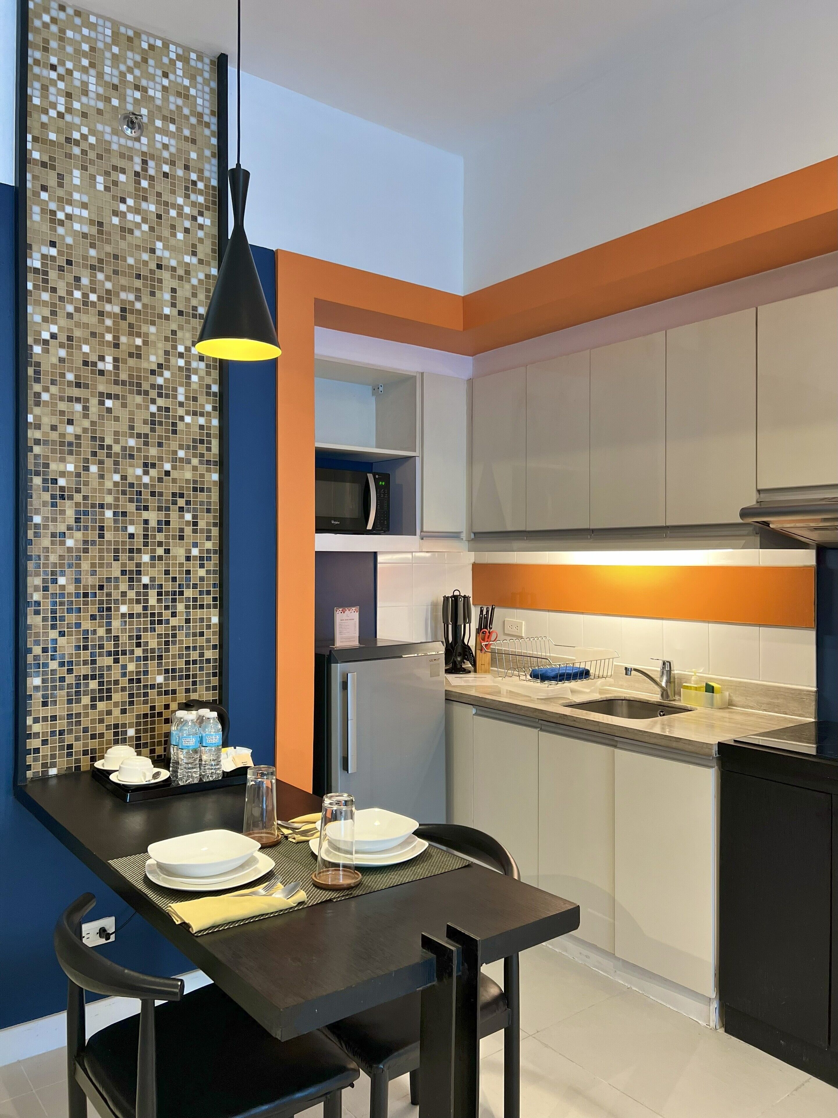 Eine moderne Küche mit Essbereich, ausgestattet mit einer Mikrowelle, Spüle und einer Wand mit Mosaikfliesen.