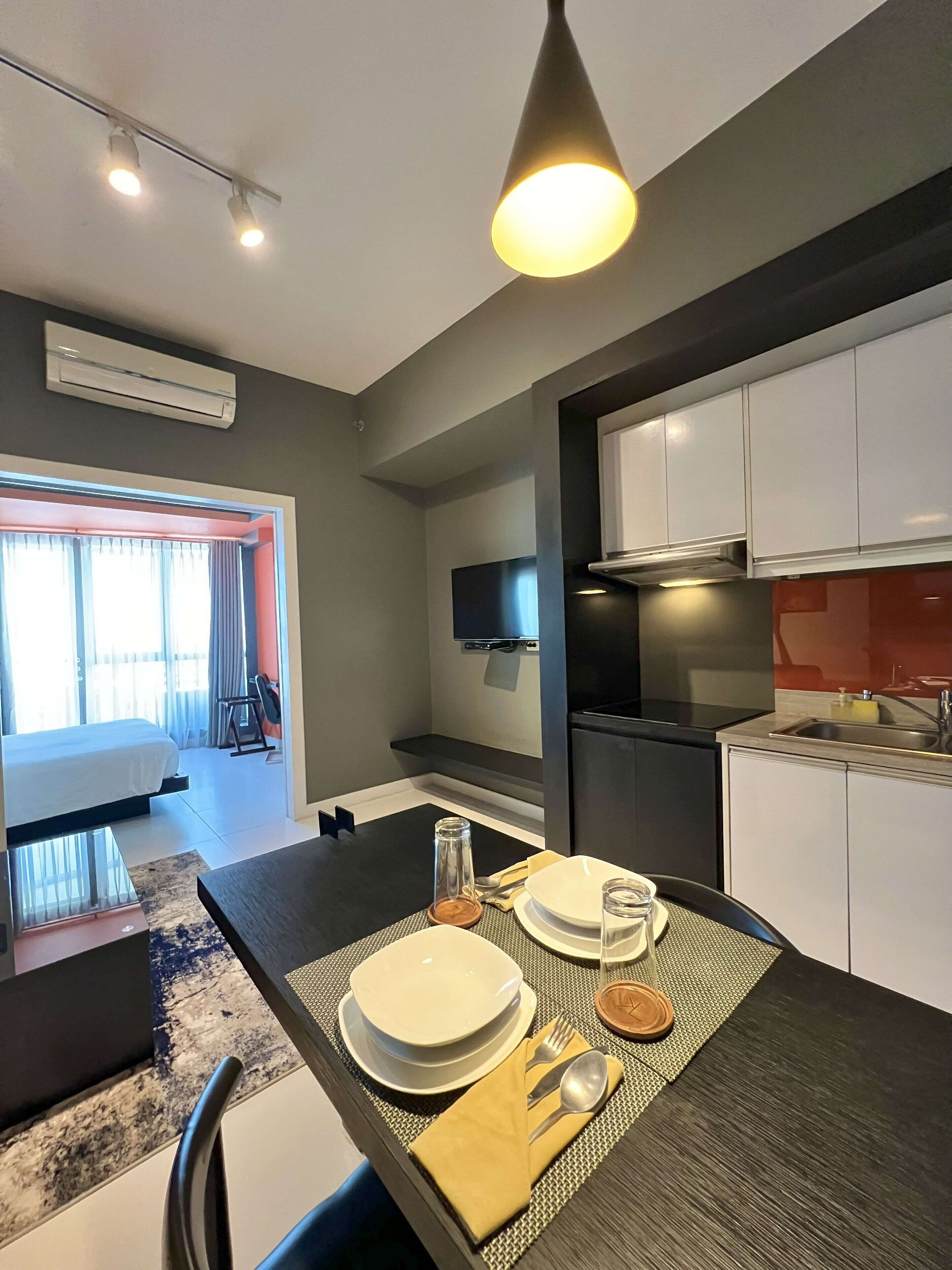 A modern hotel room with a dining area, kitchenette, and a bed with a view.