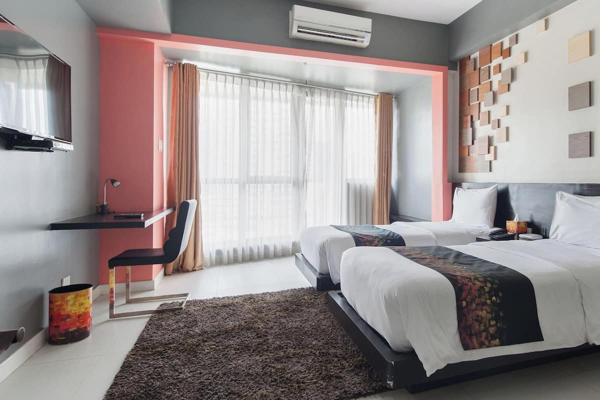 A modern hotel room with two beds, a desk, a chair, an air conditioning unit, and a large window with curtains.