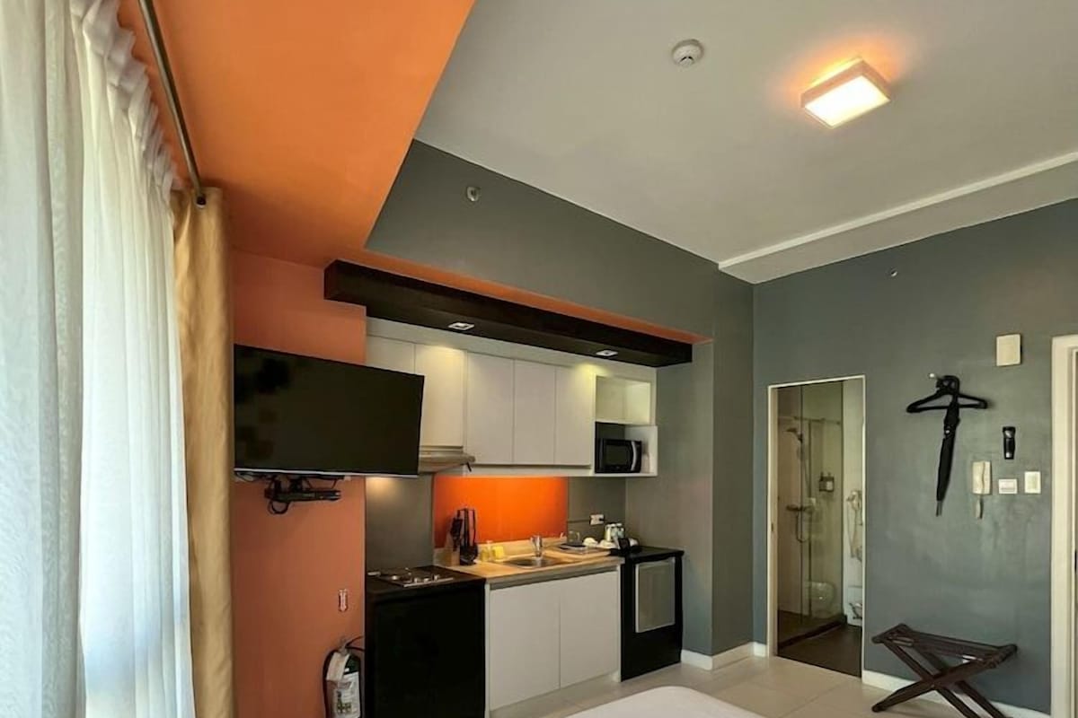 Una habitación de hotel moderna con una cama grande, kitchenette, ducha y televisor.