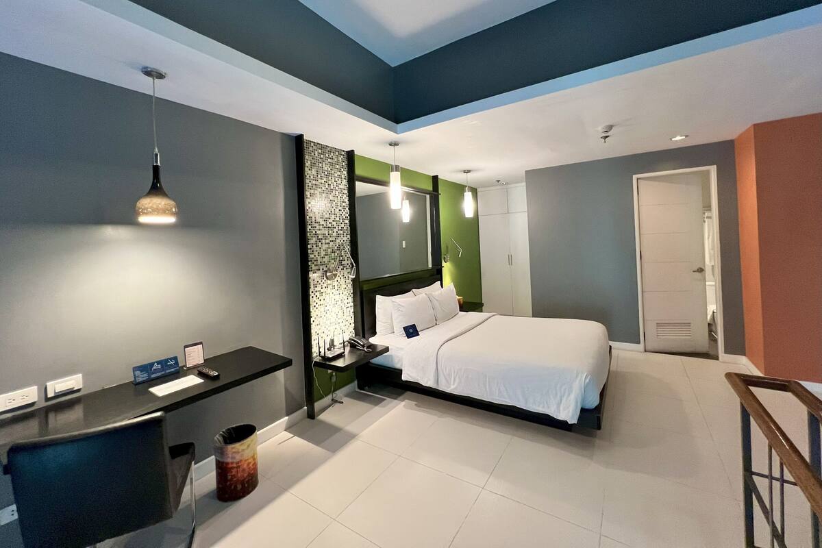 A modern hotel room with a bed, desk, and a small trash bin.