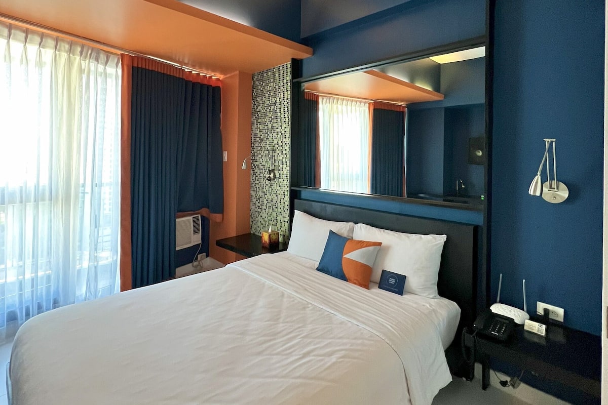 A modern hotel room with a large bed, a nightstand, a desk, and a mirror.
