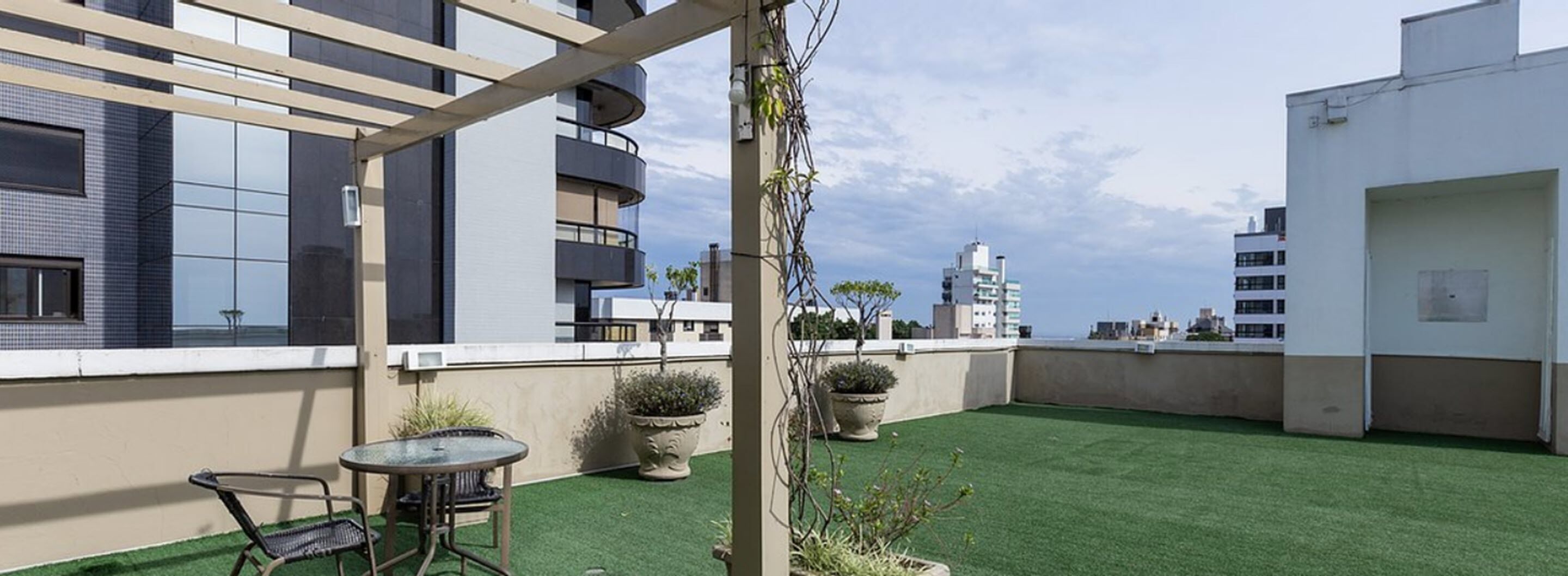 A rooftop terrace with artificial grass, potted plants, a glass table, and chairs.