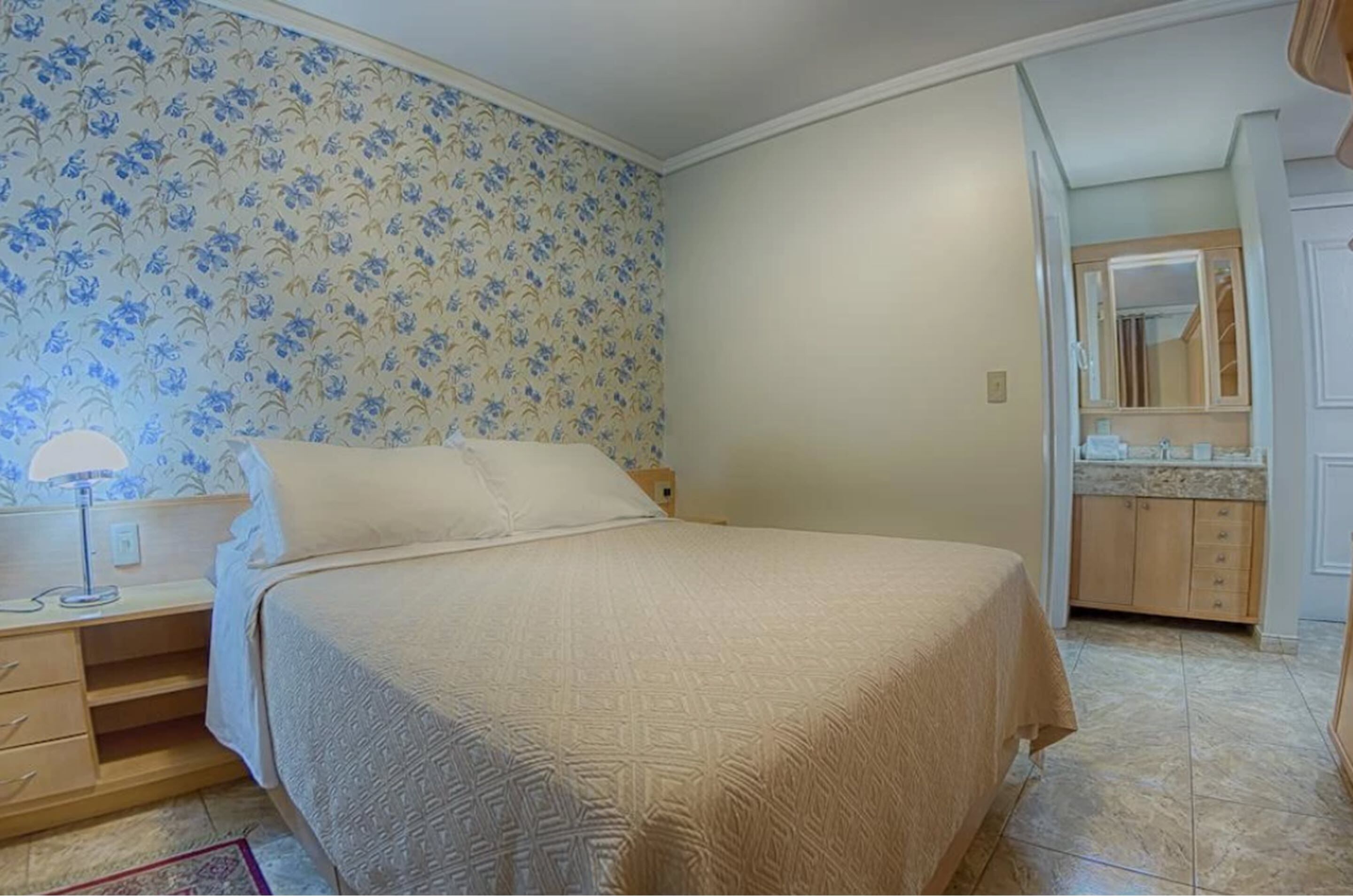 Une chambre à coucher comprenant un lit, une table de chevet, une lampe, une commode et une salle de bain avec un miroir et un lavabo.