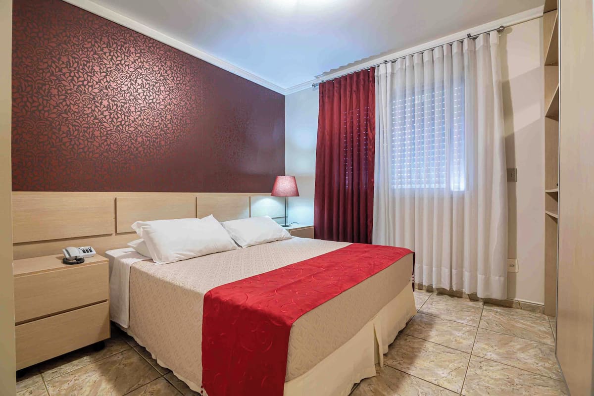 A hotel room with a bed, nightstand, and a red curtain.